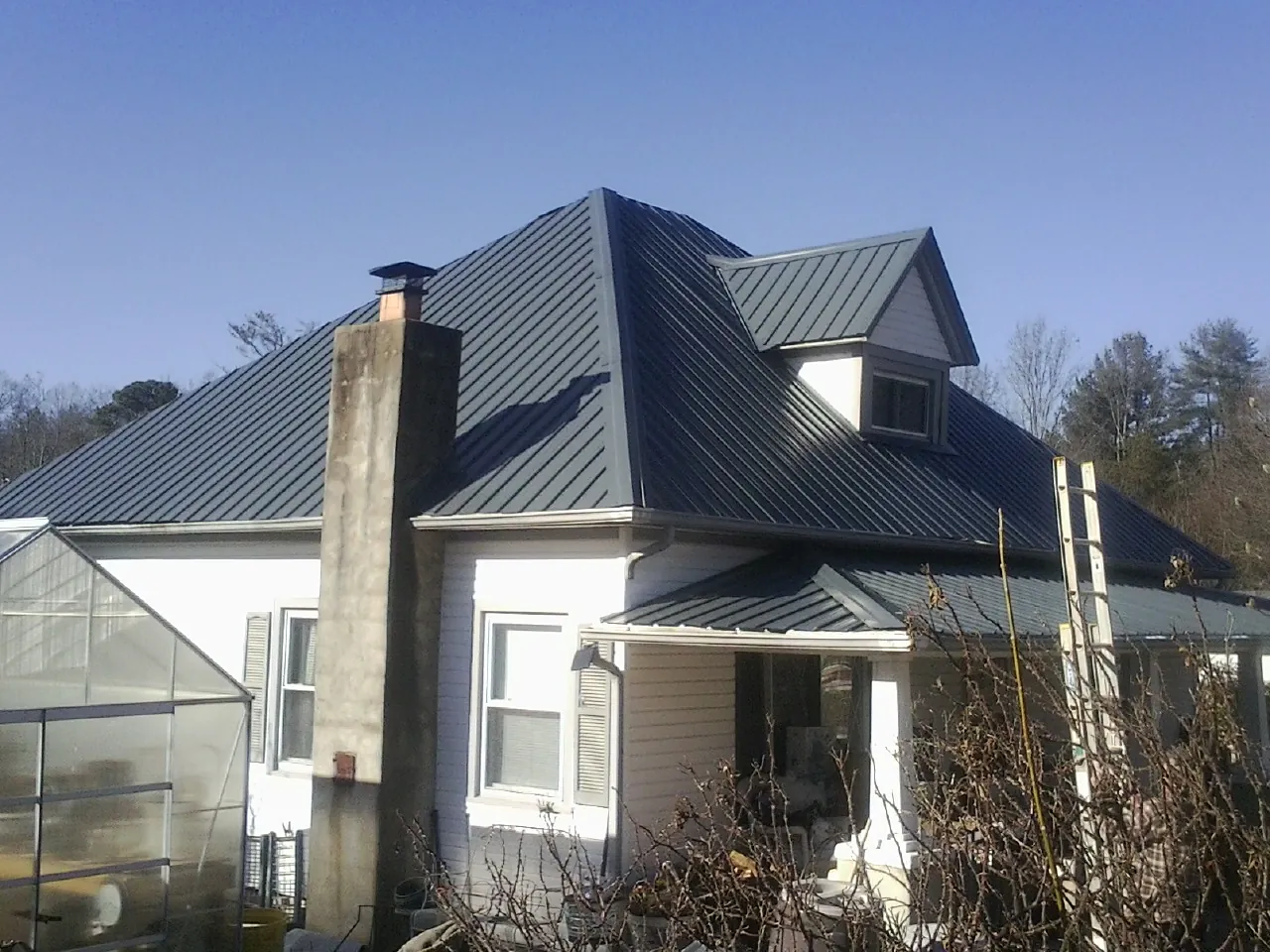 Dark blue standing seam metal roof on a white farmhouse with dormer — Slate & Tile Roof Repair by Roofing Brothers in Lacota