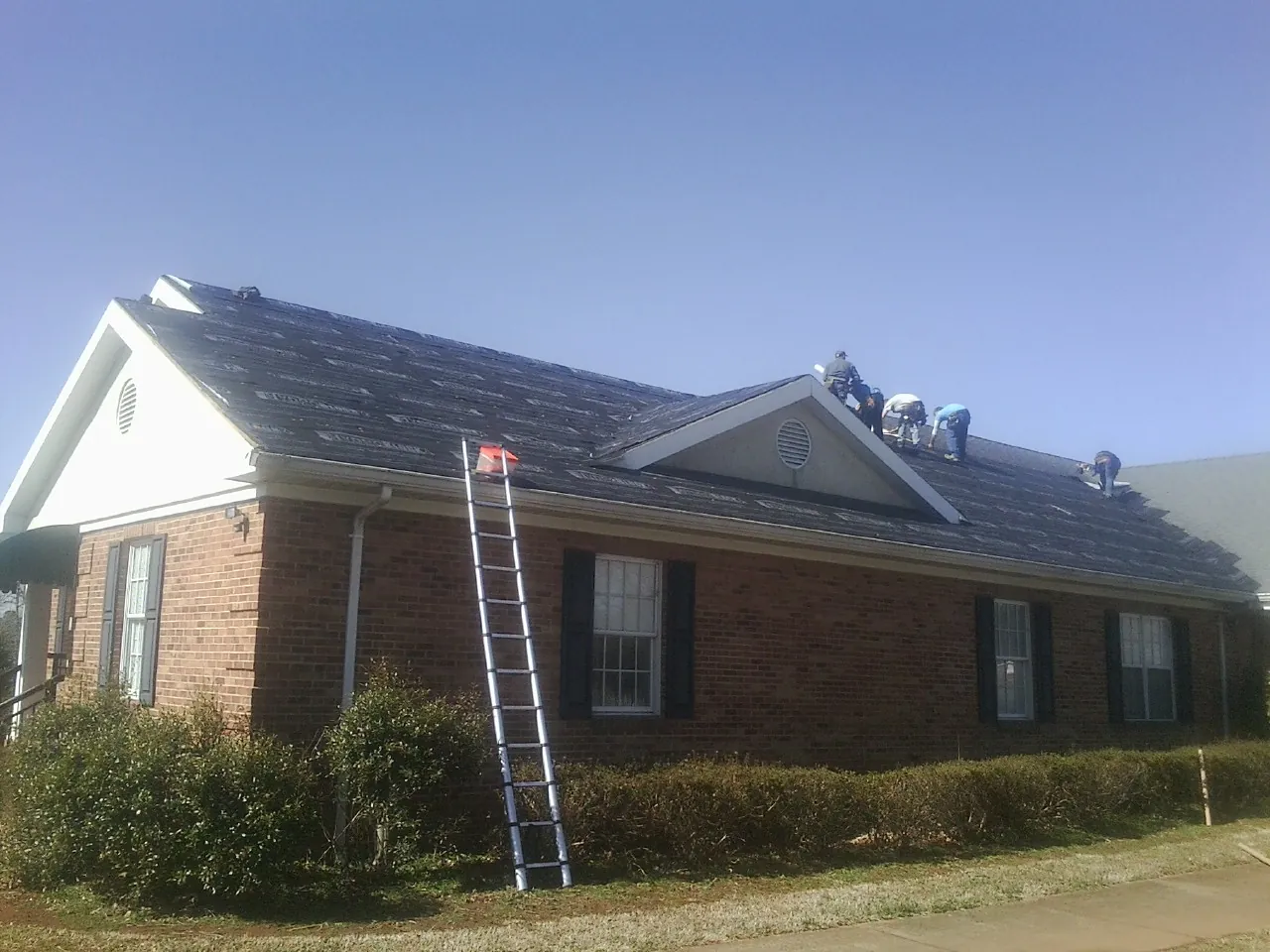 Crew tearing shingles off a brick ranch roof with a ladder set — Emergency Roof Repair work by our crew in Lacota