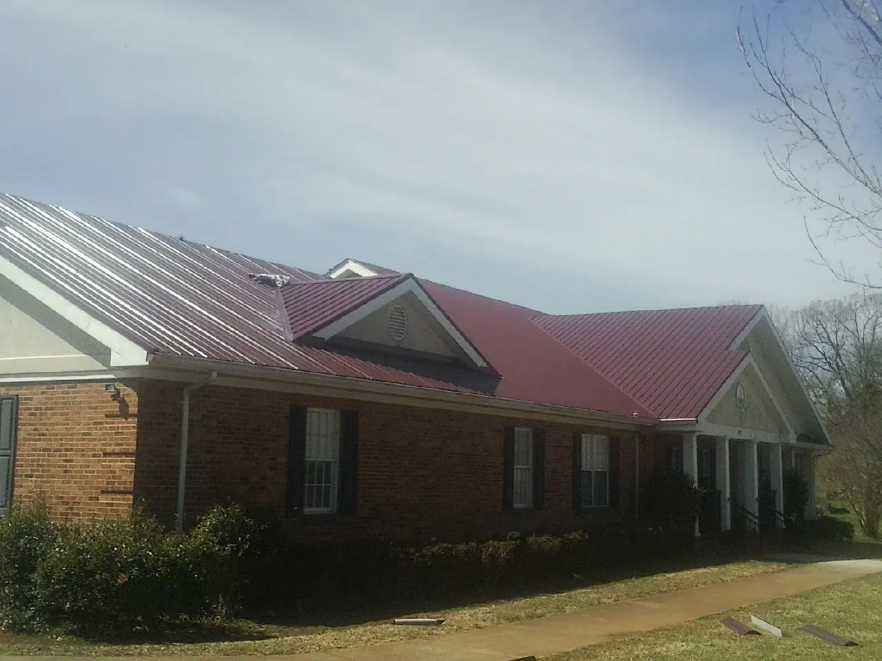 Red metal roof with gabled entries on a long brick building, from a Hail Damage Roof Repair job in Lacota