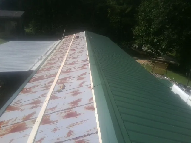 Old rusted panels beside newly installed green metal roofing — Wind Damage Roof Repair by Roofing Brothers in Lacota