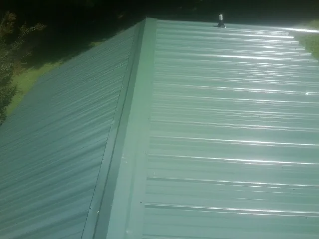 New green metal panels meeting at the ridge of a roof — Flat Roof Repair work by our crew in Lacota