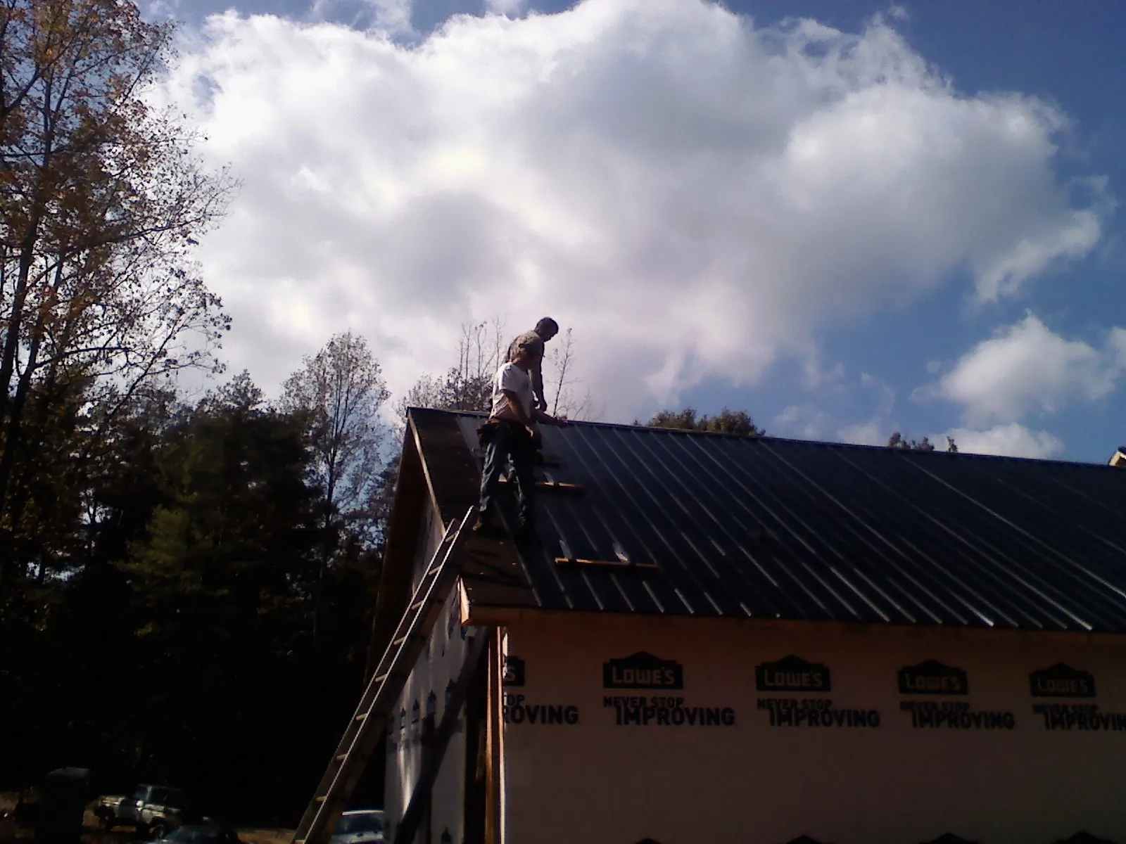 Roofer fastening dark metal panels high against a cloudy sky, from a Roof Inspection job in Lacota