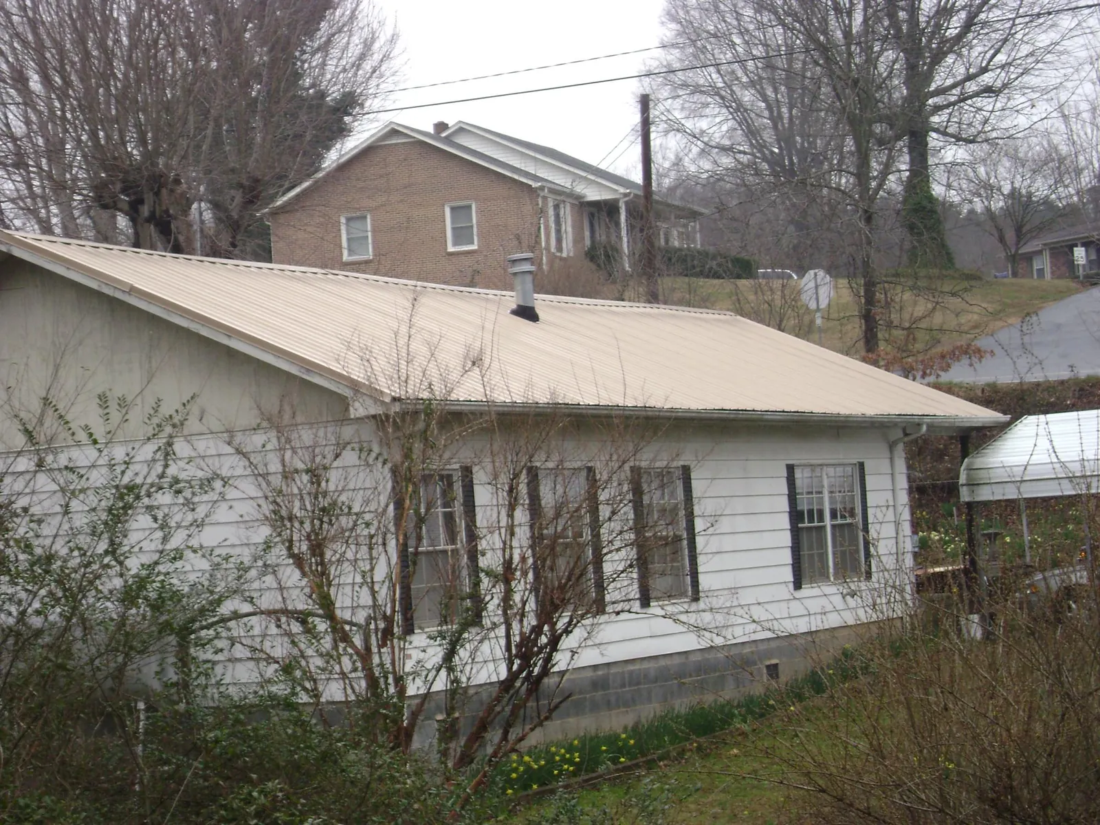 Tan metal roof on a white sided house set into a hillside — Commercial Roofing by Roofing Brothers in Lacota