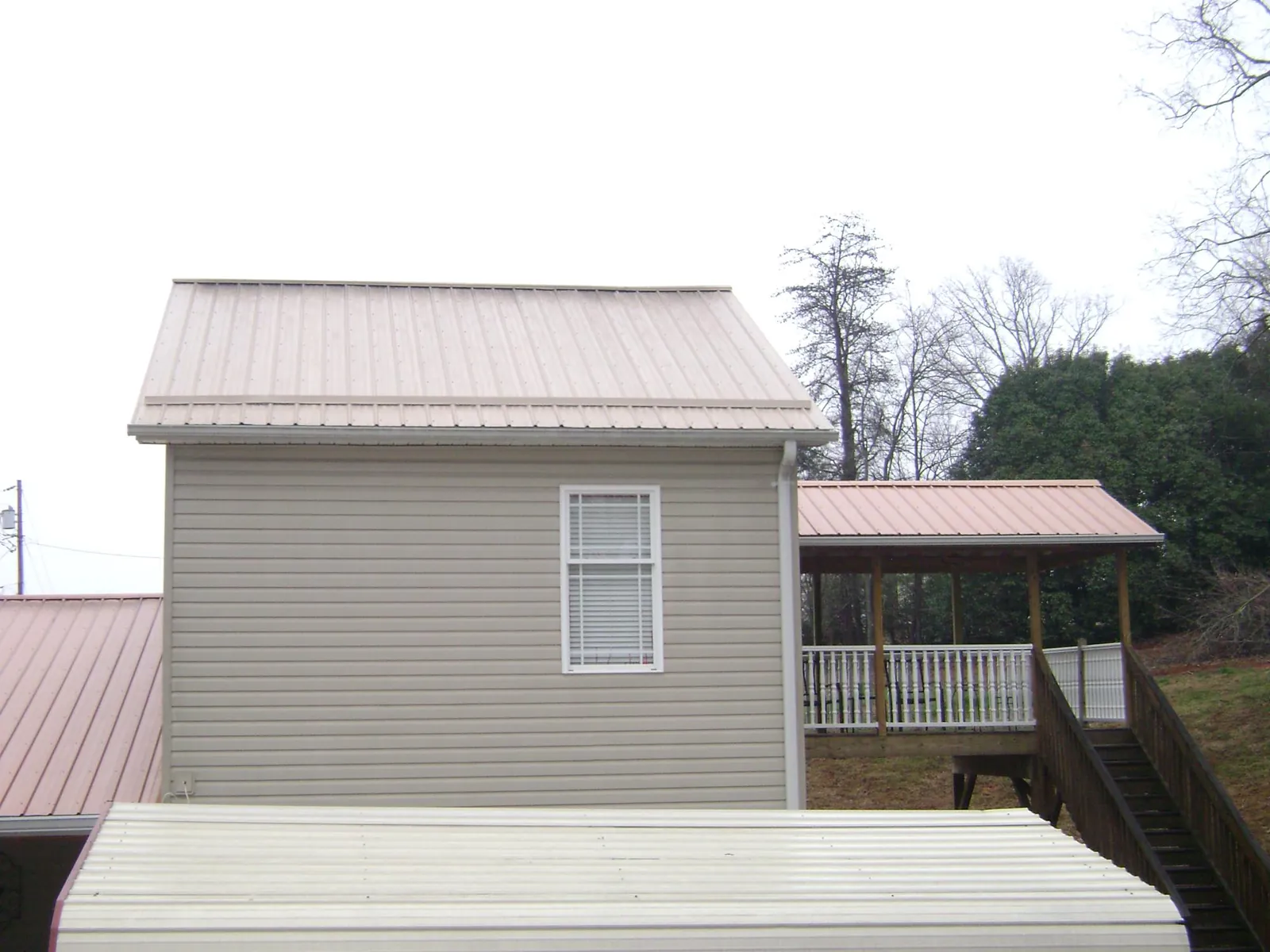 Tan metal roofs on a two story addition and attached porch, from a Roof Replacement job in Lacota